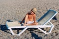 Tanned boy in hat sits on white sunbed on the beach Royalty Free Stock Photo