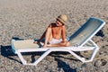 Tanned boy in hat sits on white sunbed on the beach