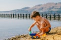 Tanned boy playing in the sand on the lake Royalty Free Stock Photo