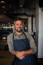 Tanned male owner smiling while leaning against bench with crossed hands in coffee shop.