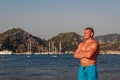 Tanned Caucasian man in blue bathing shorts stands on the beach in Turkey