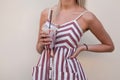 Tanned fashionable young woman in a stylish striped pink dress poses near a wall in the city and holds in hands a sweet milkshake