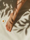 Tanned female leg with smooth skin and red nail polish on toes. Elegant foot on sand with shadows and daisy. Generative AI Royalty Free Stock Photo