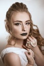 Tanned girl with black lips and arrows with light curly hair and professional bright makeup, isolates on white in a silk white