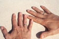 Tanned hands of newlyweds with gold rings on ring fingers on white sand as a symbol of wedding travel Royalty Free Stock Photo