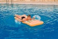 Tanned and happy boy floating on an inflatable mattress in an outdoor pool