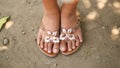 Tanned legs of a little girl in slates with a decorative butterfly. Girl barefoot in summer shoes on sand. Philippines.