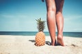 Tanned legs of young woman standing with pineapple at tropical beach in summer. Royalty Free Stock Photo