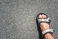 Tanned male legs in hiking sandals on the asphalt on a sunny day.