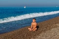 Tanned nine-year-old boy in bathing fits sits back on the pebble shore of the sea Royalty Free Stock Photo