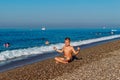 Tanned nine-year-old boy in bathing fits sits back on the pebble shore of the sea Royalty Free Stock Photo