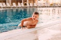 Tanned seven-year-old Caucasian boy holding the rim in the outdoor pool Royalty Free Stock Photo