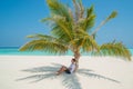 Tanned sexy man wearing white t-shirt and black shorts relaxing under palm tree at tropical sandy beach at island luxury resort Royalty Free Stock Photo