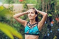 A tanned, slender woman in a swimsuit, posing in the refreshing tropical rain, smoothing her hair with her hands. Summer vacation