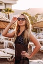 Tanned smiling young woman in sunglasses stands on the beach in the contoured sunlight