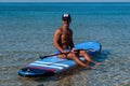 Tanned sporty man sits on his surfboard on the water and looks to the sea. The concept is a sporty and healthy lifestyle