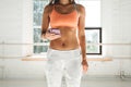 Tanned sporty woman wearing sportwear in white sunny gym hold smartphone in hand and counts calories in fitness application fater