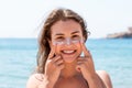 Tanned woman protects her face with sun cream from sunburn at the beach