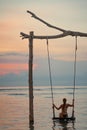 Tanned woman riding on a swing standing in the water. Sunset and sea in the background. Relax and vacation concept. Free and trip Royalty Free Stock Photo