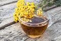 Tansy infusion in a glass cup on a wooden table. Tansy Herbal tea. Healing herbs