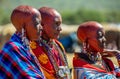 Three Masai women stand in the background of the village.