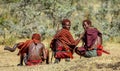 Three young Masai warriors in traditional clothes and weapons are sitting in the savannah.