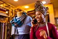 tanzanian woman with snake print turban over hear working in fabrics shop calling to client by smartphone