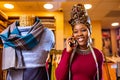 tanzanian woman with snake print turban over hear working in fabrics shop calling to client by smartphone