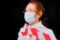 Tape-bound woman with painful eyes in a protective mask on a dark background, profile portrait. Close-up of a red-haired girl in a