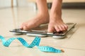 Tape in front of woman standing on floor scales. Overweight problem