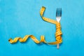 Tape measure around a fork as concept for diet. Fork are wrapped in yellow measuring tape on blue background. Copy space for text Royalty Free Stock Photo