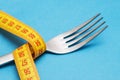 Tape measure around a fork as concept for diet. Fork are wrapped in yellow measuring tape on blue background Royalty Free Stock Photo