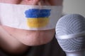 Tape over his mouth with the flag of Ukraine, trying to speak into a microphone