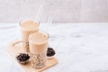 Tapioca pearl ball bubble milk tea, popular Taiwan drink, in drinking glass with straw on marble white table and wooden tray,