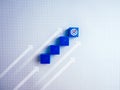 Target dart, goal icon on top of blue cube block as steps with rising up arrows, 3d blocks chart on line graph pattern paper