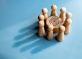 Target icon on round wood block surrounded with small wooden human figures made a crown shadow shape. Royalty Free Stock Photo