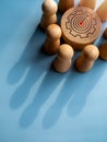 Target icon on round wood block surrounded with small wooden human figures made a crown shape shadow. Royalty Free Stock Photo