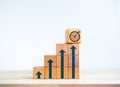 Target icon on wooden cube on top of wood blocks bar graph chart steps with blue rising arrows symbol on desk. Royalty Free Stock Photo