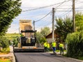 Targoviste, Romania - 2019. Workers operating asphalt paver machine during road construction on a sunny day. Construction of a new