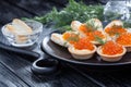 Tartlets with butter and red caviar and dill on the black plate