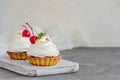 Tartlets with cherry filling and Italian meringue with a cocktail cherry on top on a board on a concrete background. Royalty Free Stock Photo