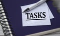 TASKS - word in a white notebook against the background of a black notebook with a pen