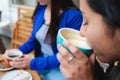 Taste of Serenity: Close-Up Shot of a Latina Woman Enjoying a Coffee at the Patio of a Cozy Cafe with a friend.