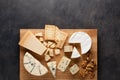 Tasting cheese dish on a wooden plate. Food for wine and romantic, cheese delicatessen on a dark stone table. Top view Royalty Free Stock Photo