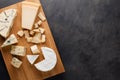 Tasting cheese dish on a wooden plate. Food for wine and romantic, cheese delicatessen on a dark stone table. Top view Royalty Free Stock Photo