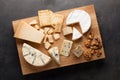 Tasting cheese dish on a wooden plate. Food for wine and romantic, cheese delicatessen on a dark stone table. Top view Royalty Free Stock Photo