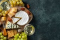 Tasting cheese dish on a wooden plate. Food for wine and romantic date, cheese delicatessen on a black concrete background. Top