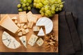 Tasting cheese dish on a wooden plate. Food for wine and romantic, cheese delicatessen on a dark stone table. Top view Royalty Free Stock Photo