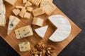 Tasting cheese dish on a wooden plate. Food for wine and romantic, cheese delicatessen on a dark stone table. Top view Royalty Free Stock Photo