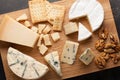 Tasting cheese dish on a wooden plate. Food for wine and romantic, cheese delicatessen on a dark stone table. Top view Royalty Free Stock Photo